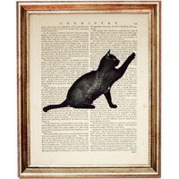 Playful black cat reaching upward, silhouette-style artwork on an old dictionary book page