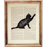 Playful black cat reaching upward, silhouette-style artwork on an old dictionary book page